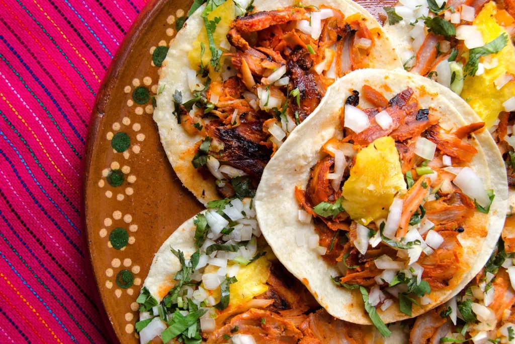 Tacos al Pastor: inspirado no shawarma libanês, consiste em carne de porco marinada, servida em tortilhas finas com cebola, coentro e um pedaço de abacaxi no topo. 